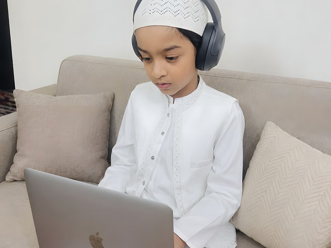 A young student following his lesson on a laptop, headphones on